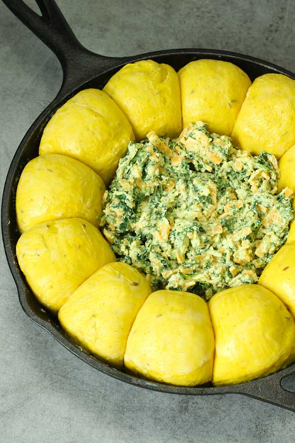 uncooked curry bread buns in a skillet with cheese spinach dip in the center