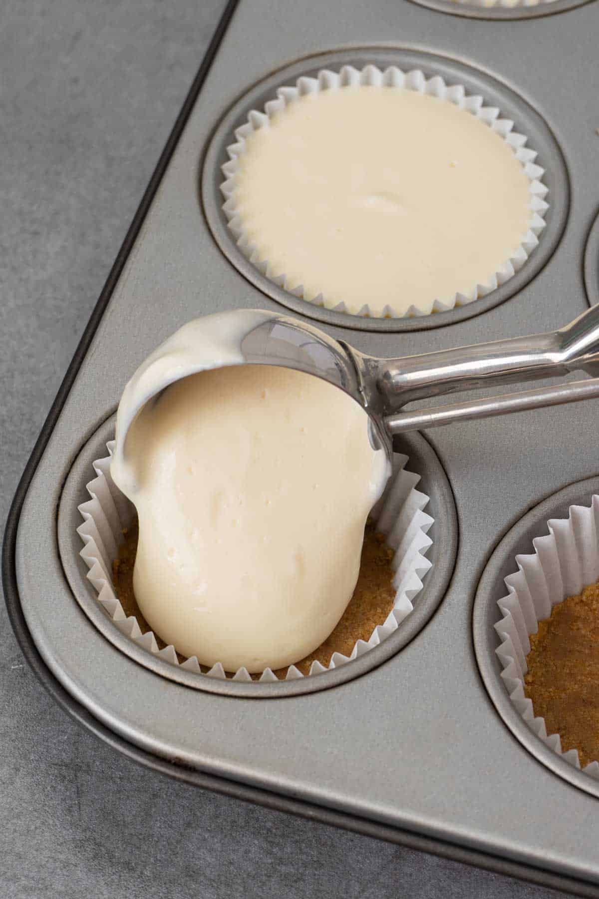 Pouring mini cheesecake batter in a muffin tin