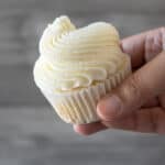 holding a cupcake with white frosting
