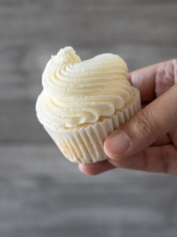 holding a cupcake with white frosting