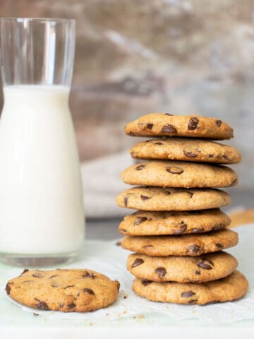 stacked chocolate chip cookies with a glass of milk