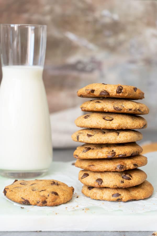 stacked chocolate chip cookies with a glass of milk