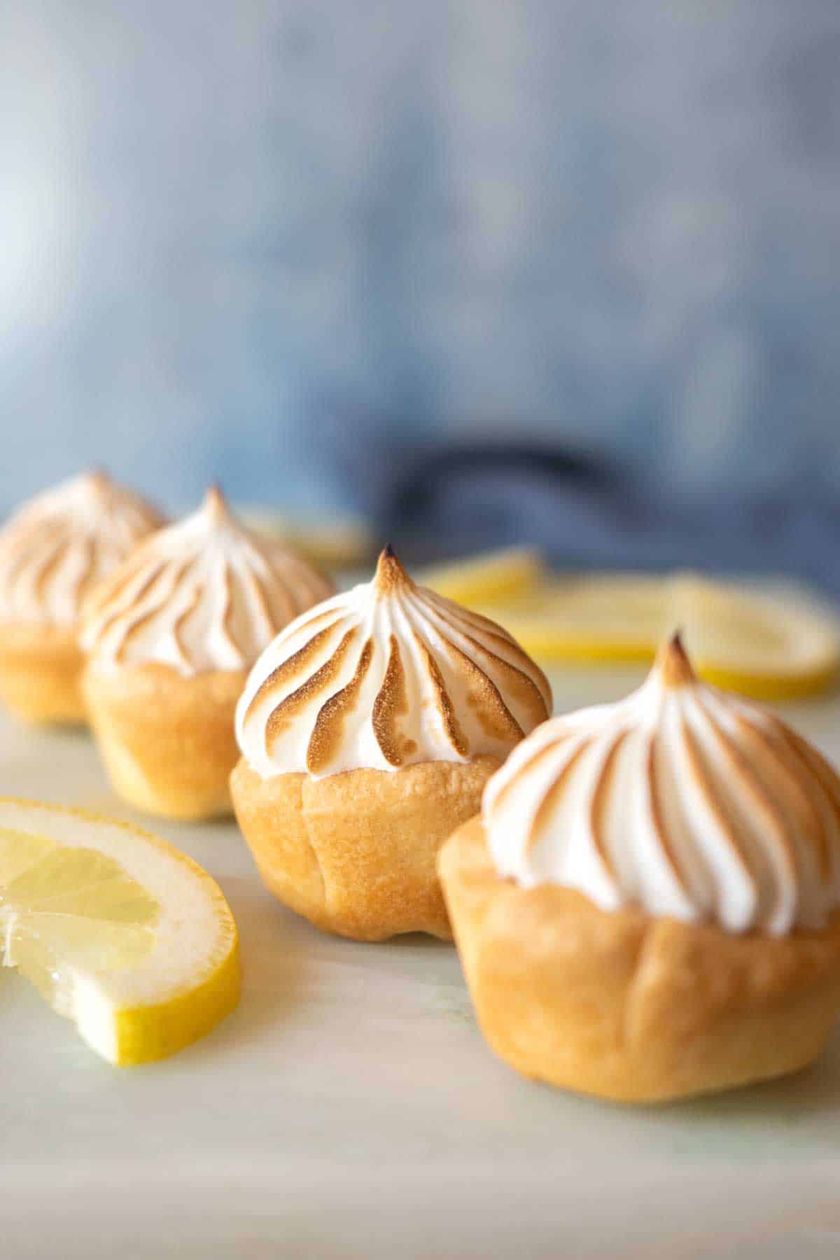 lemon meringue pie bites lined on a marble table with lemon slices