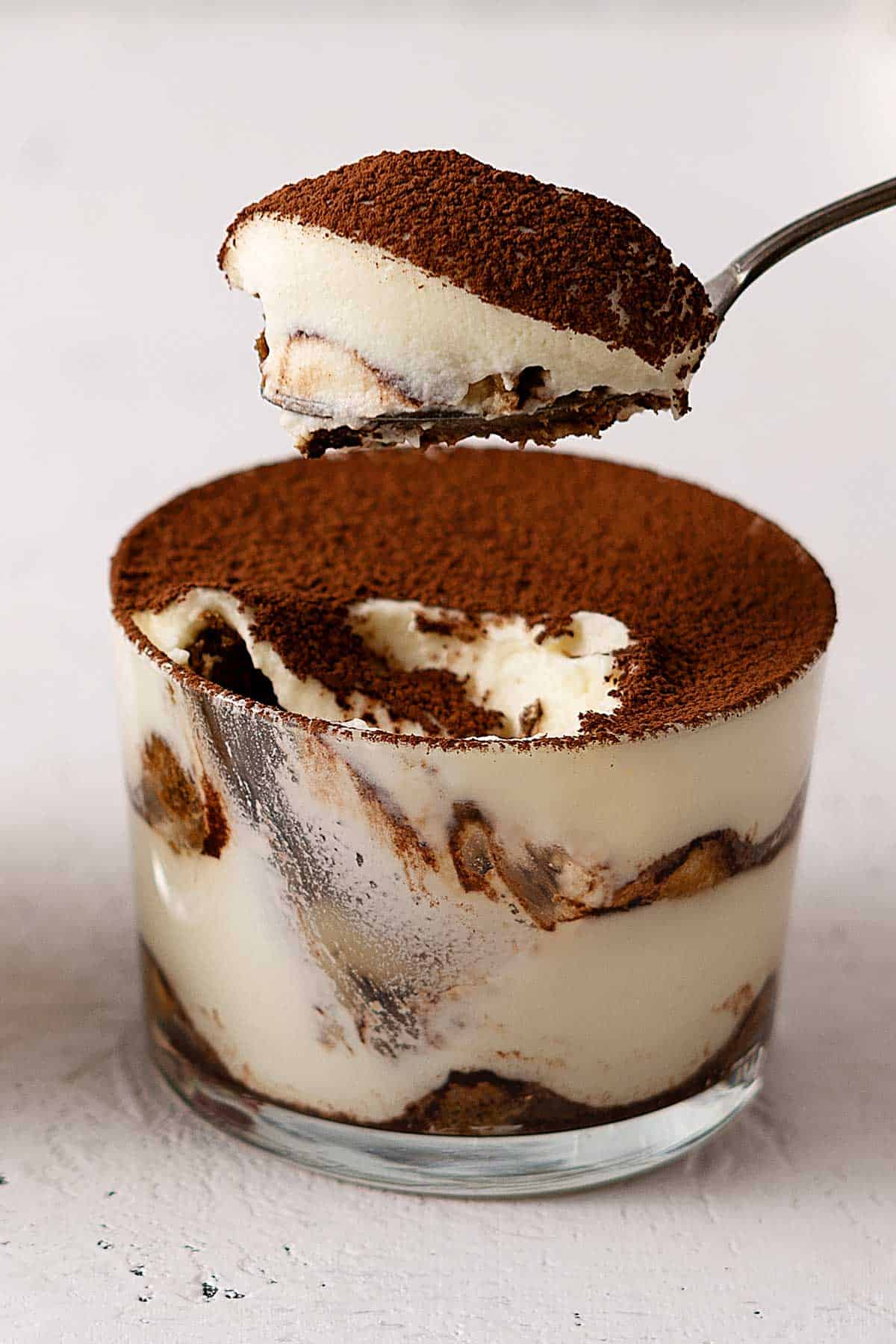 scooping tiramisu from a glass with a spoon.