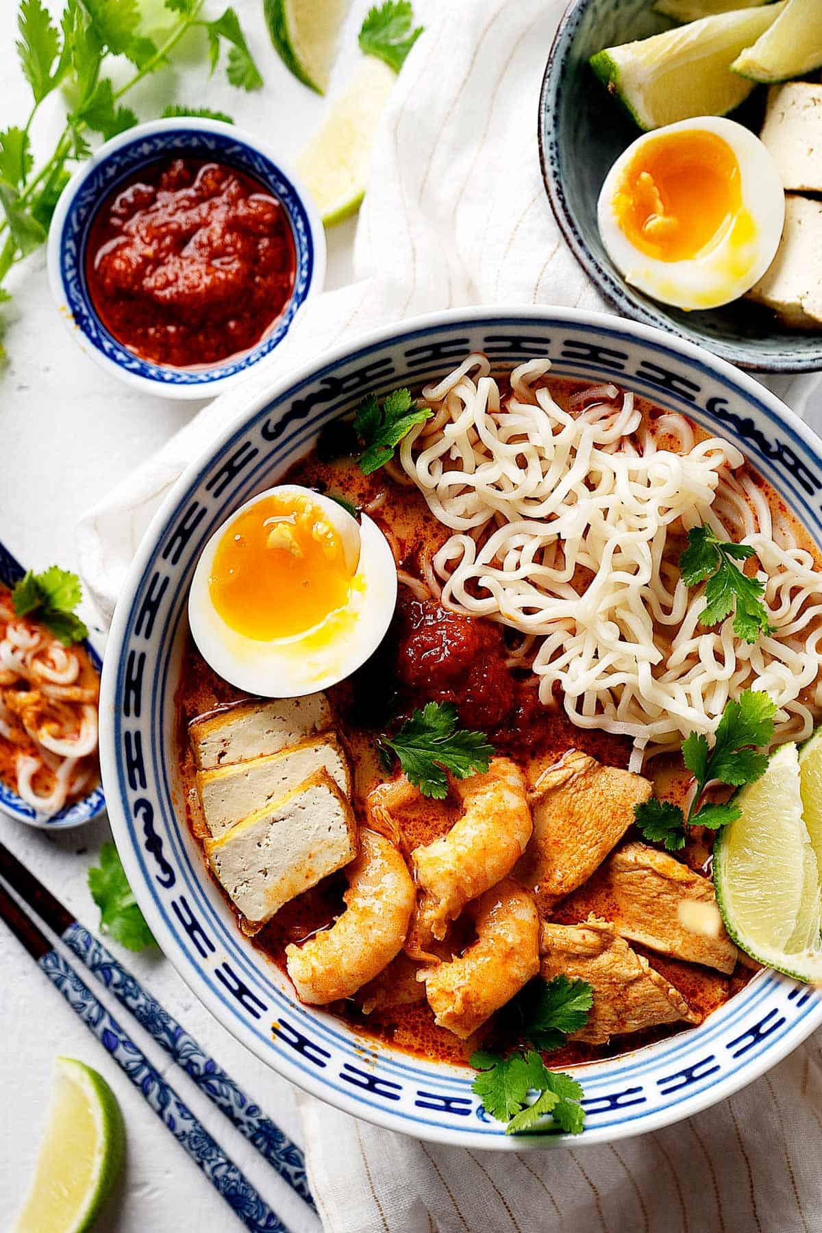 View from top of quick red curry laksa in a bowl with condiments on the side