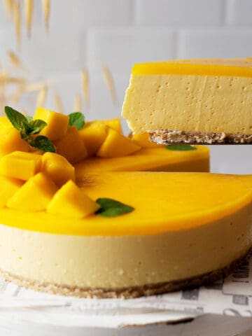 Taking a slice of healthy no bake mango cheesecake from a cake stand