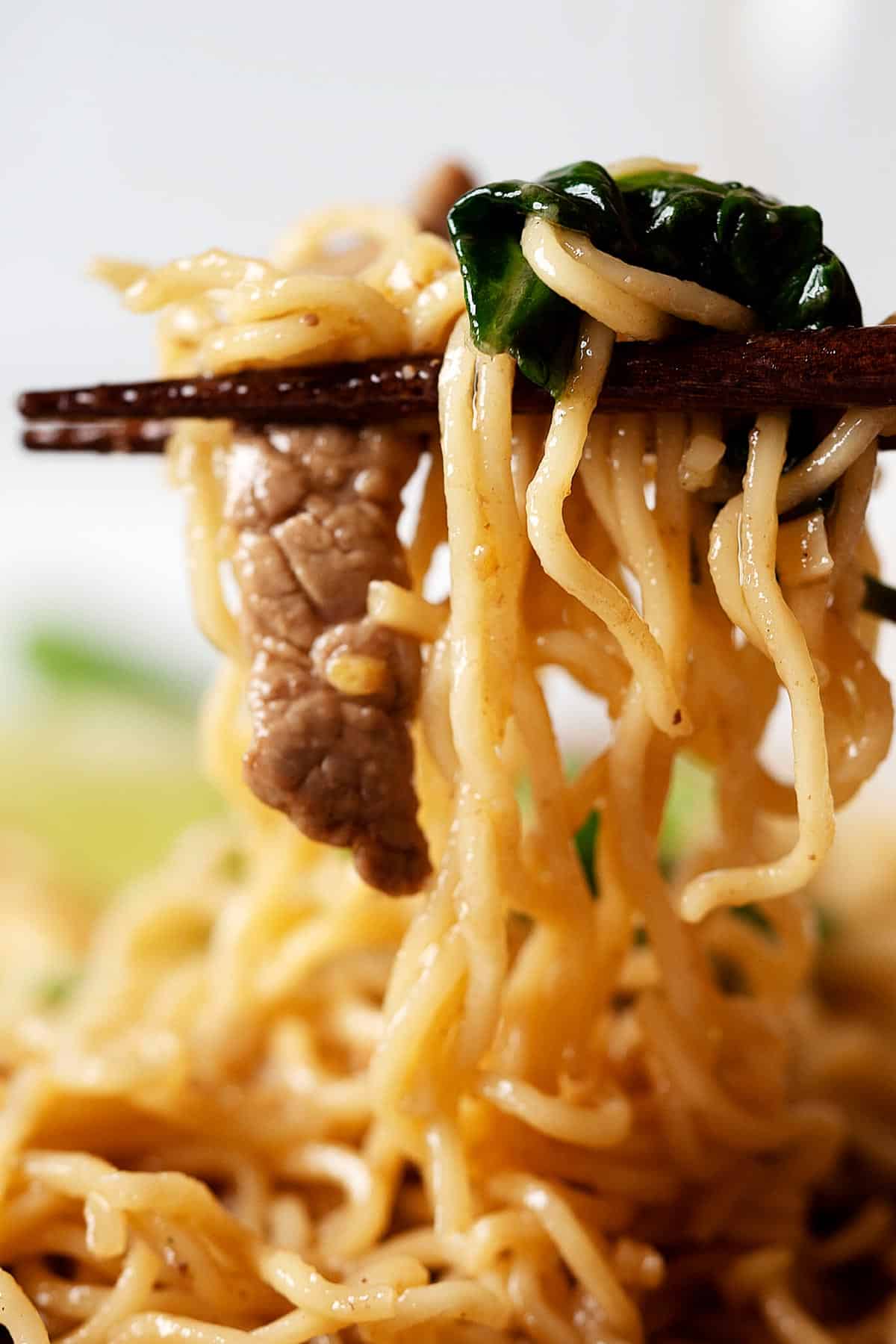 Holding some lo mein noodles with chopsticks
