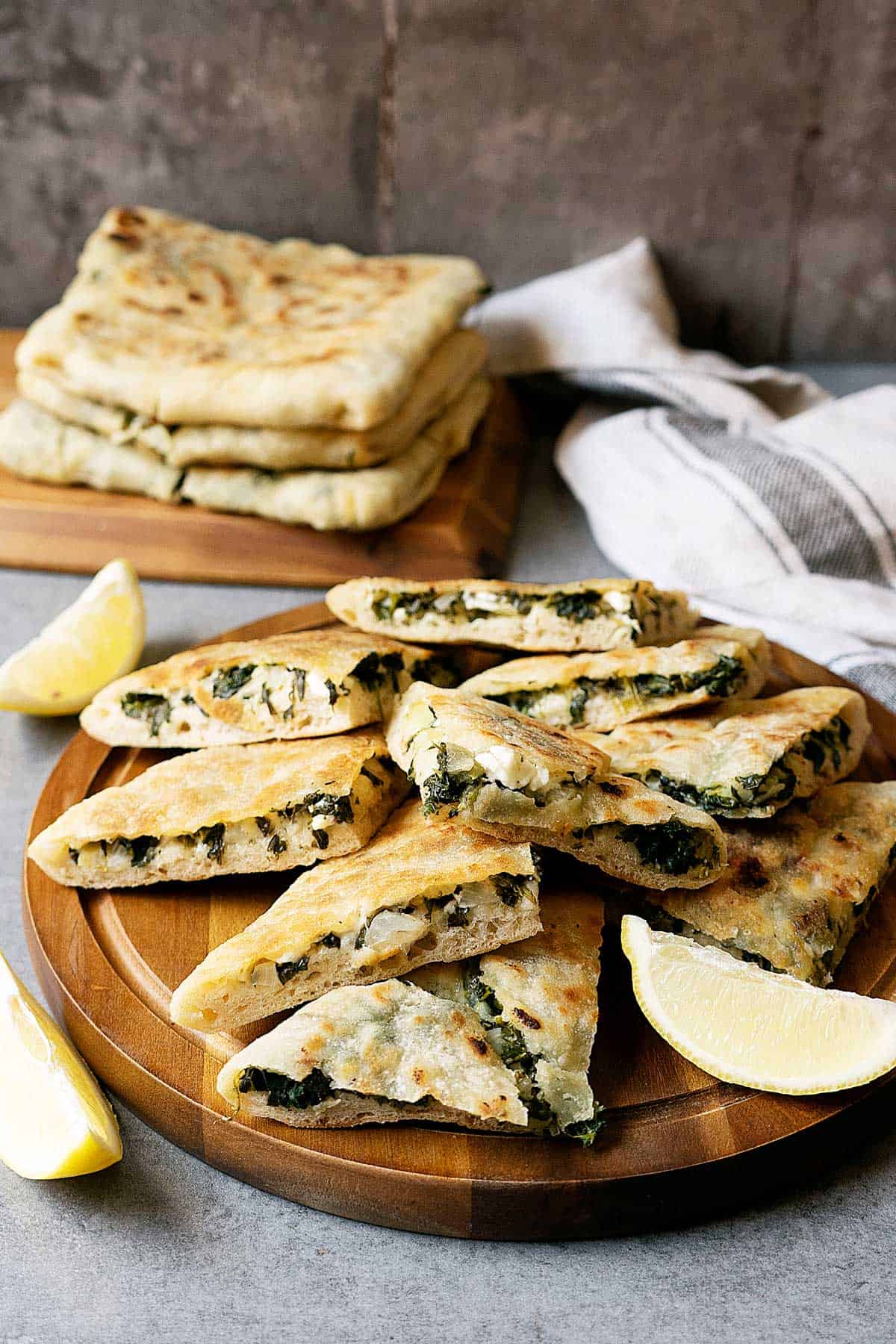 Some slices of spinach and feta gozleme on a wooden table with wedges on lemon