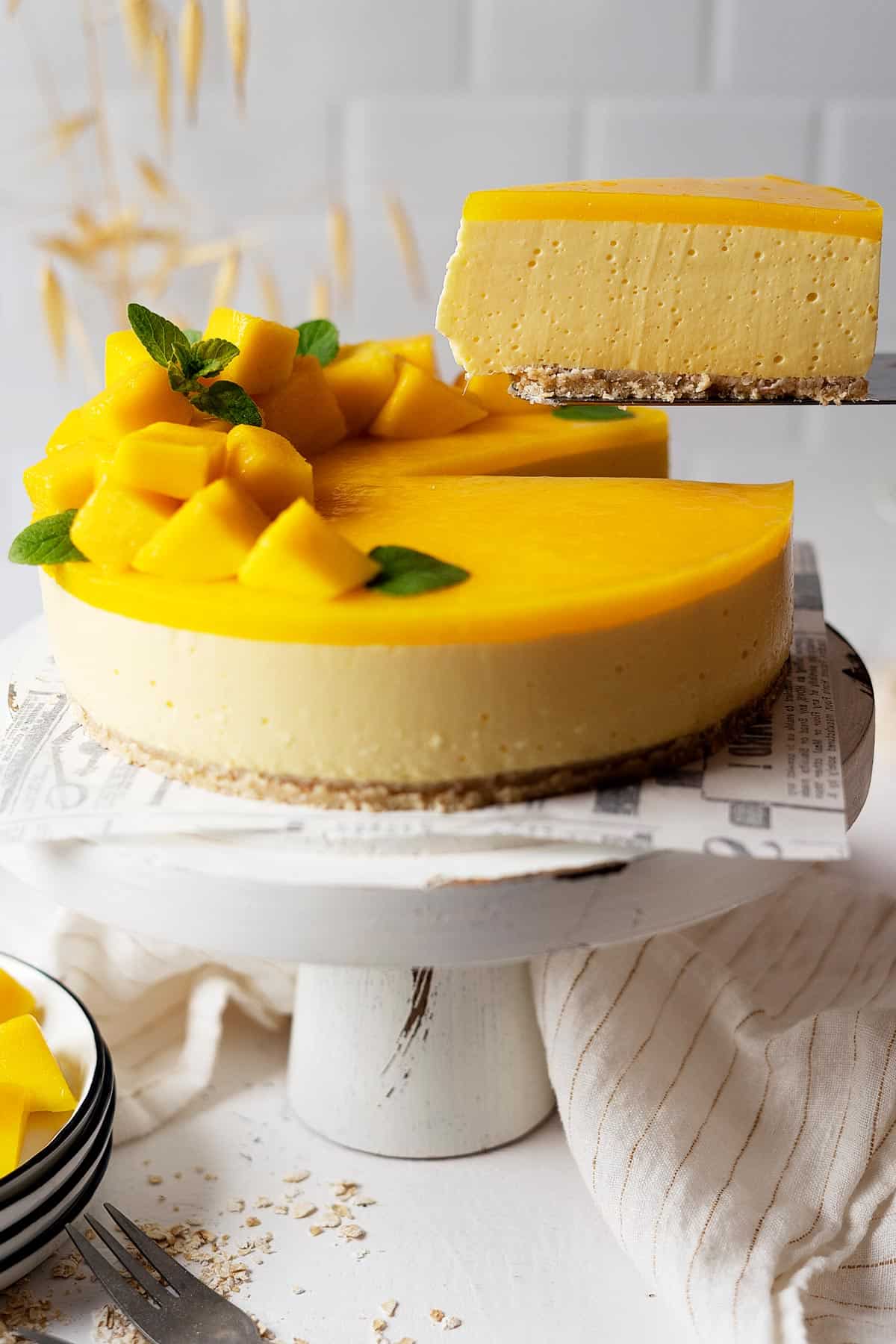 Taking a slice of healthy no bake mango cheesecake from a cake stand