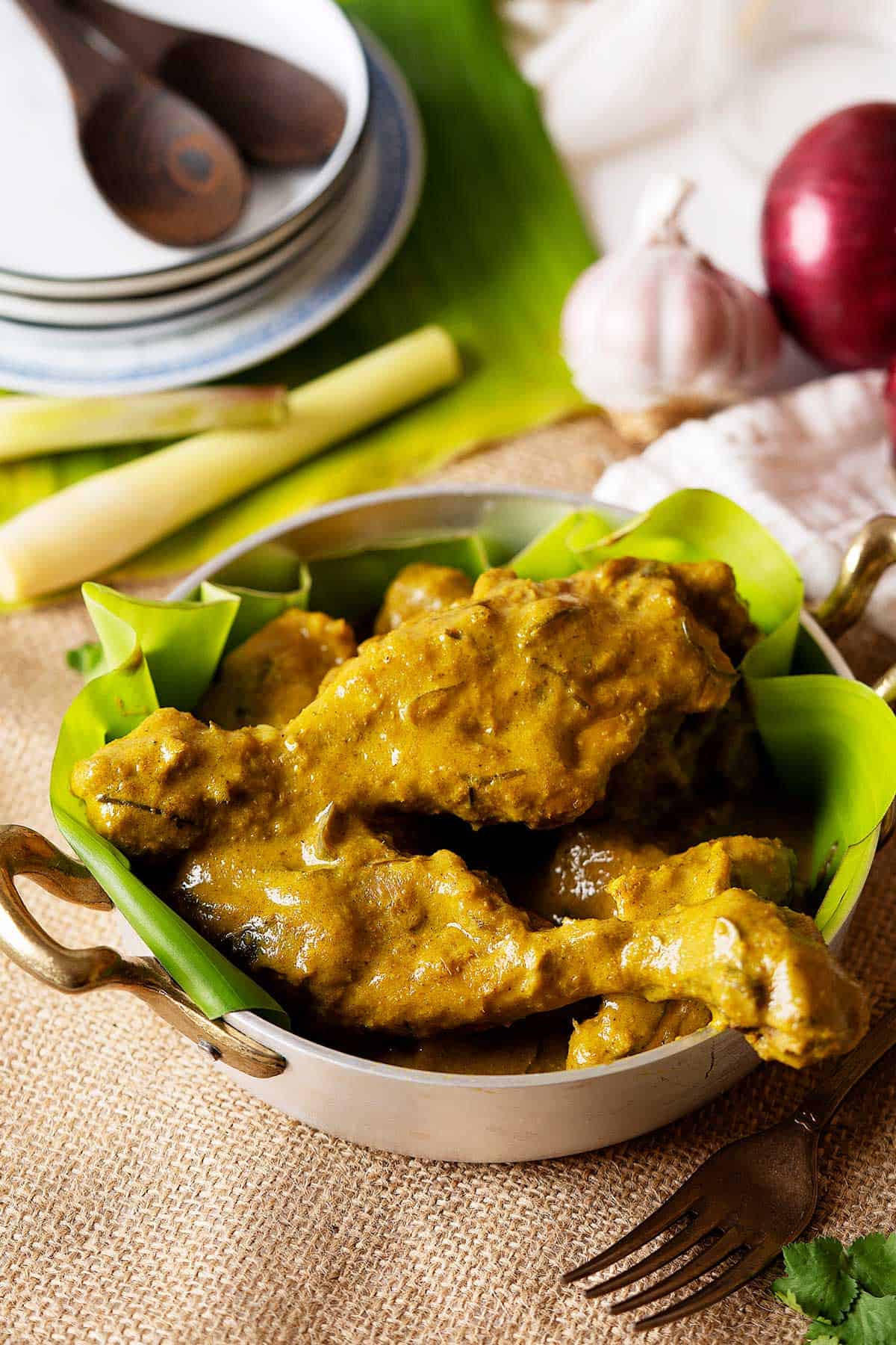 Slow cooker chicken rendang in a plate with some onions and plates at the back