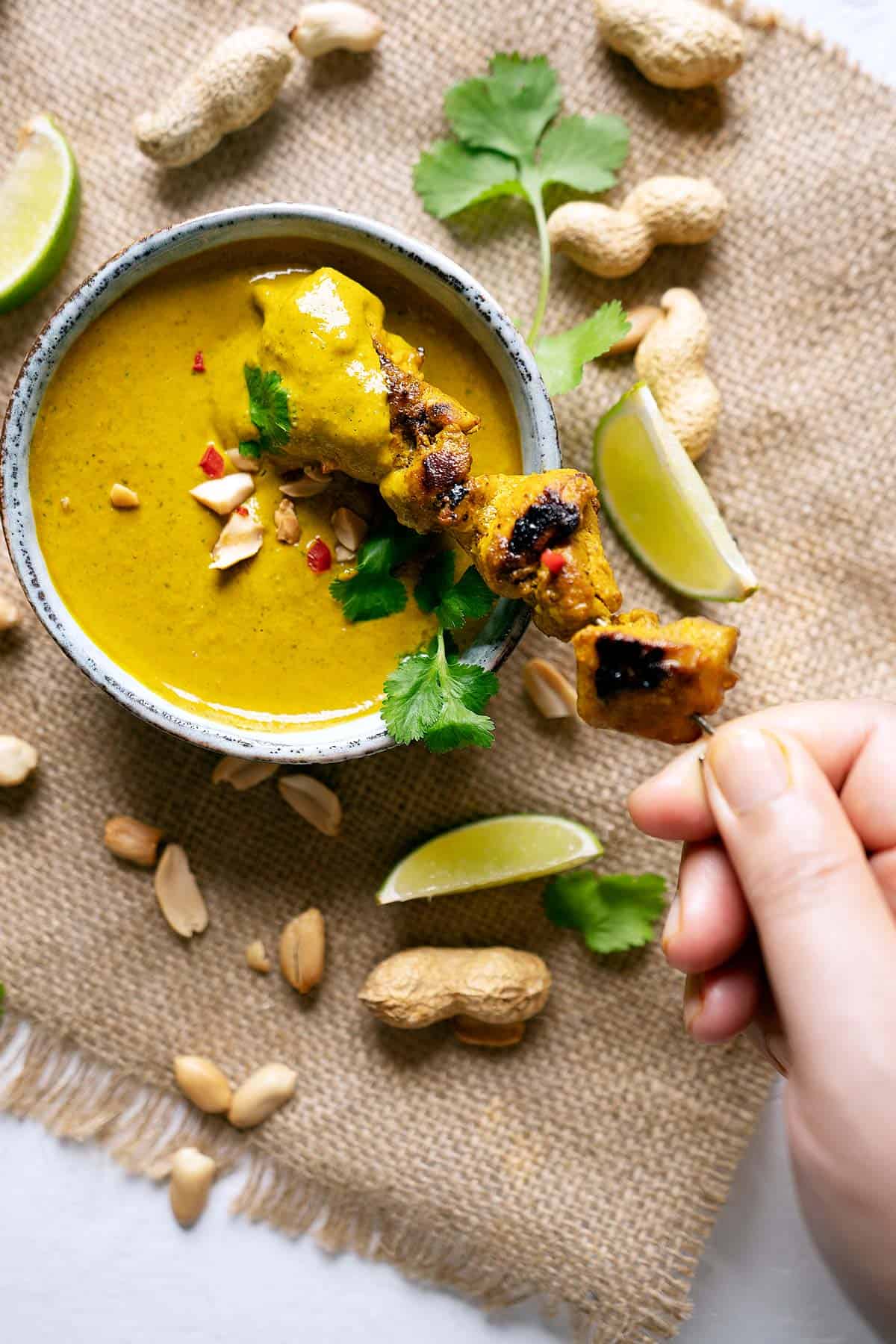 Dipping chicken satay into peanut satay sauce in a bowl