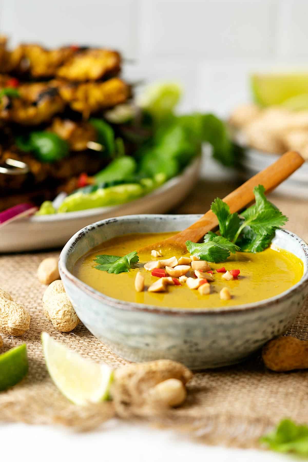 Peanut satay sauce in a bowl with some chicken satay in the background