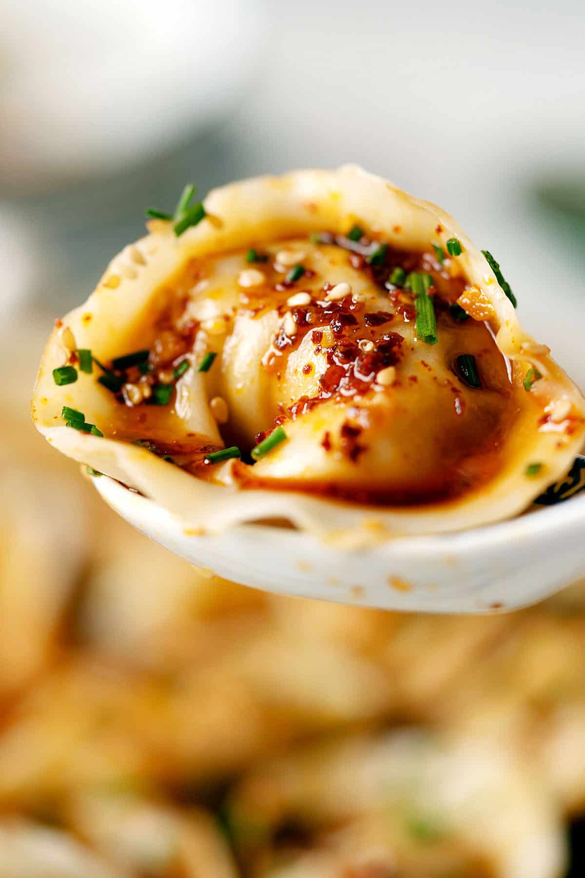 Close up of a wonton with garlic chili oil in a spoon
