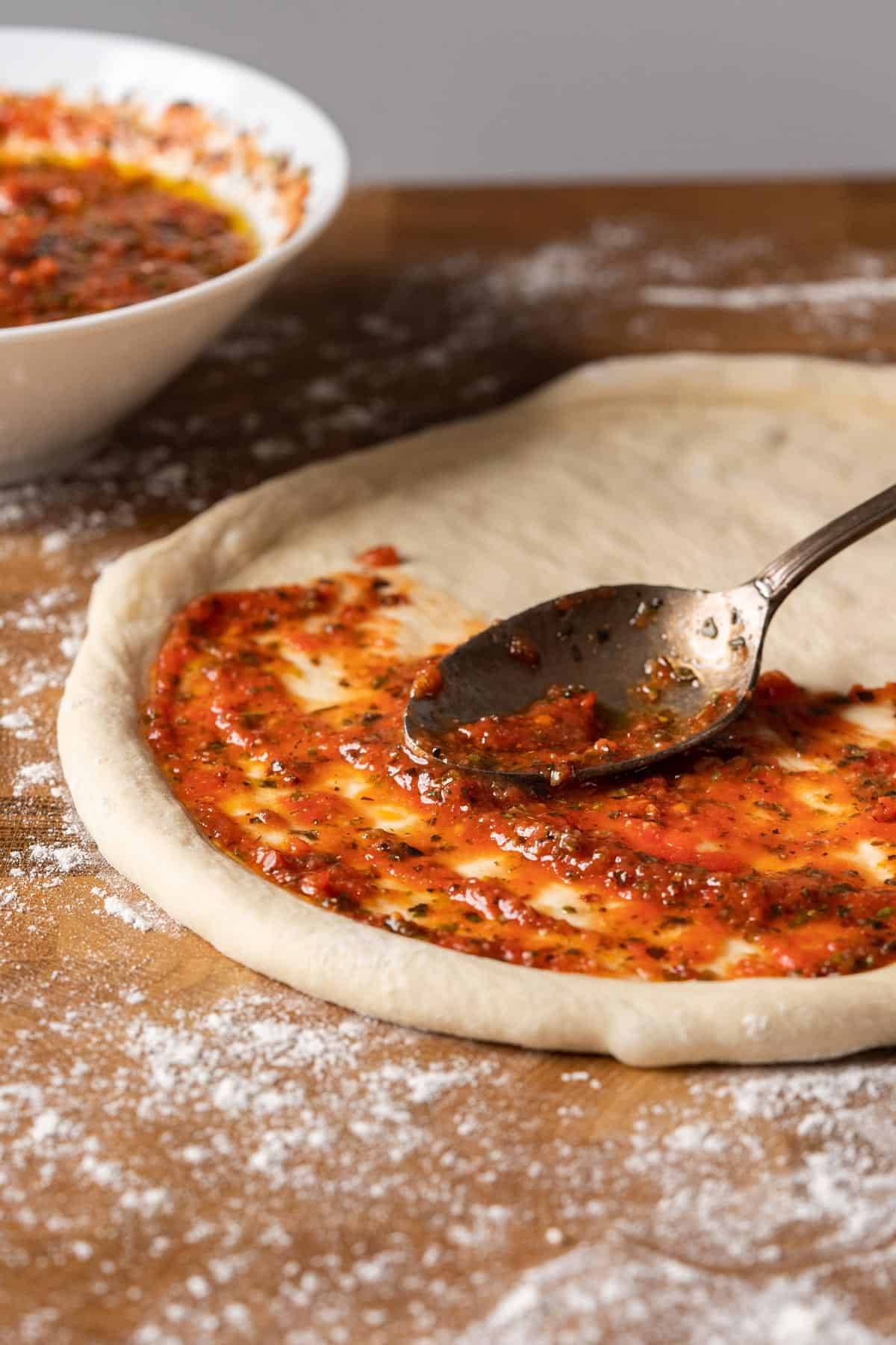 Spreading 2-minute no cook pizza sauce on a pizza dough