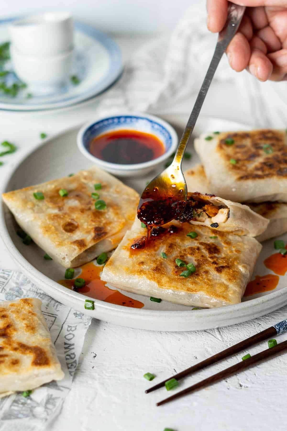 Pouring chili garlic oil on crispy rice paper dumplings.