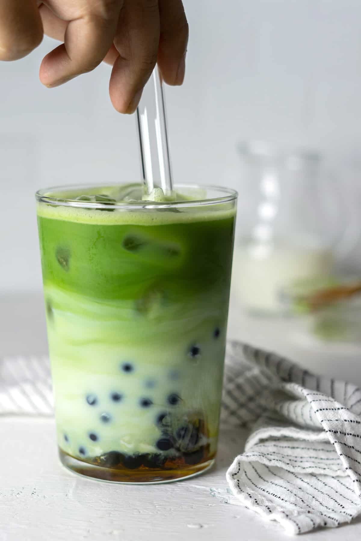 Stirring matcha boba tea with a glass straw.