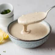 Spooning tahini sauce from a bowl.