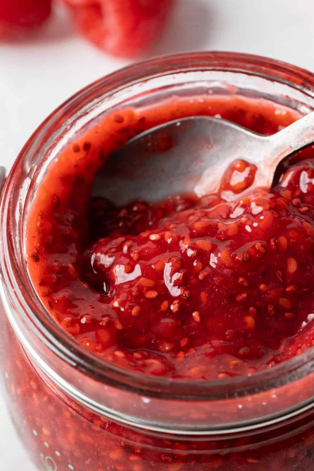 Spooning raspberry chia seed jam from a jar.