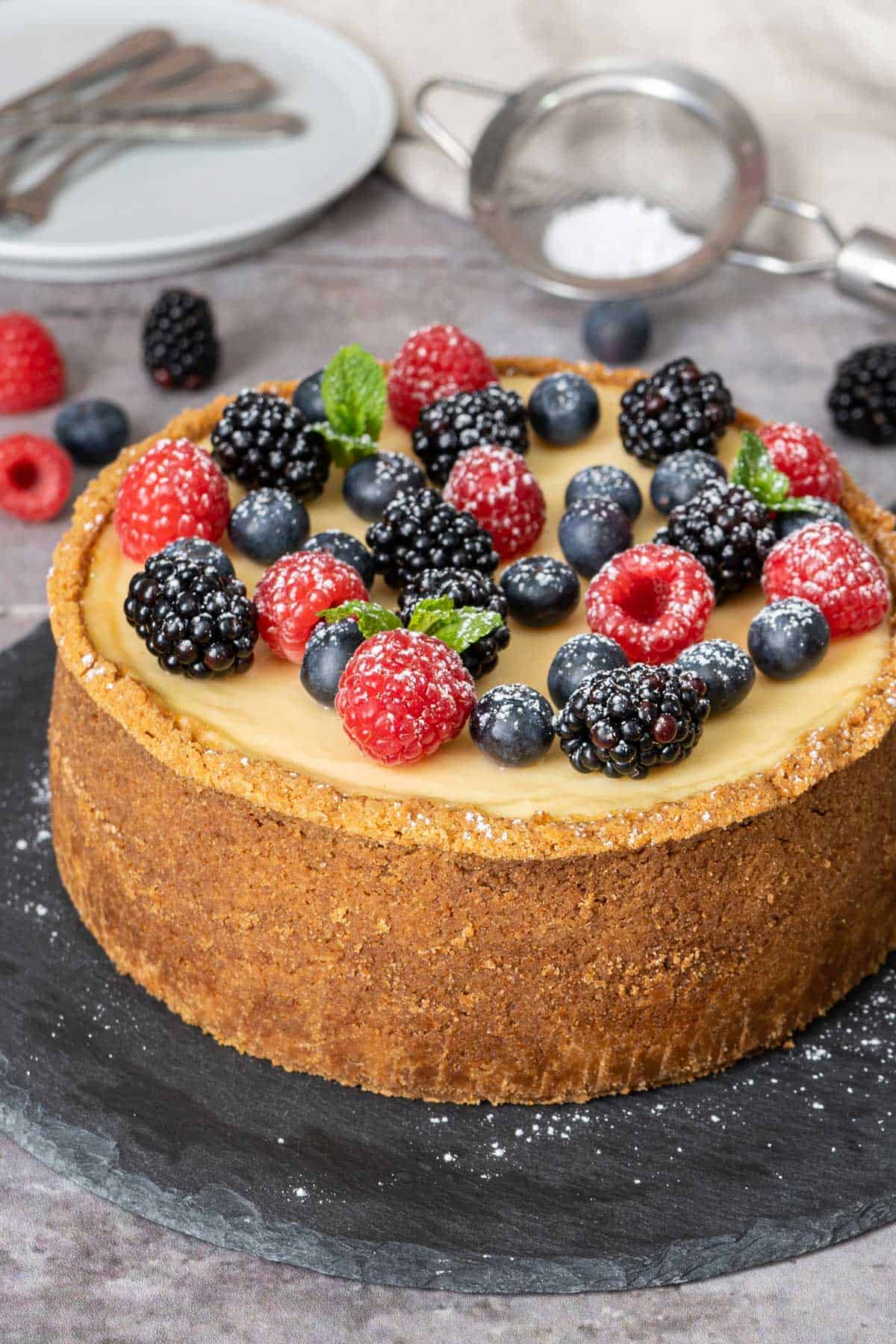 complete cooked cheesecake with mixed berries on a flat dark surface.