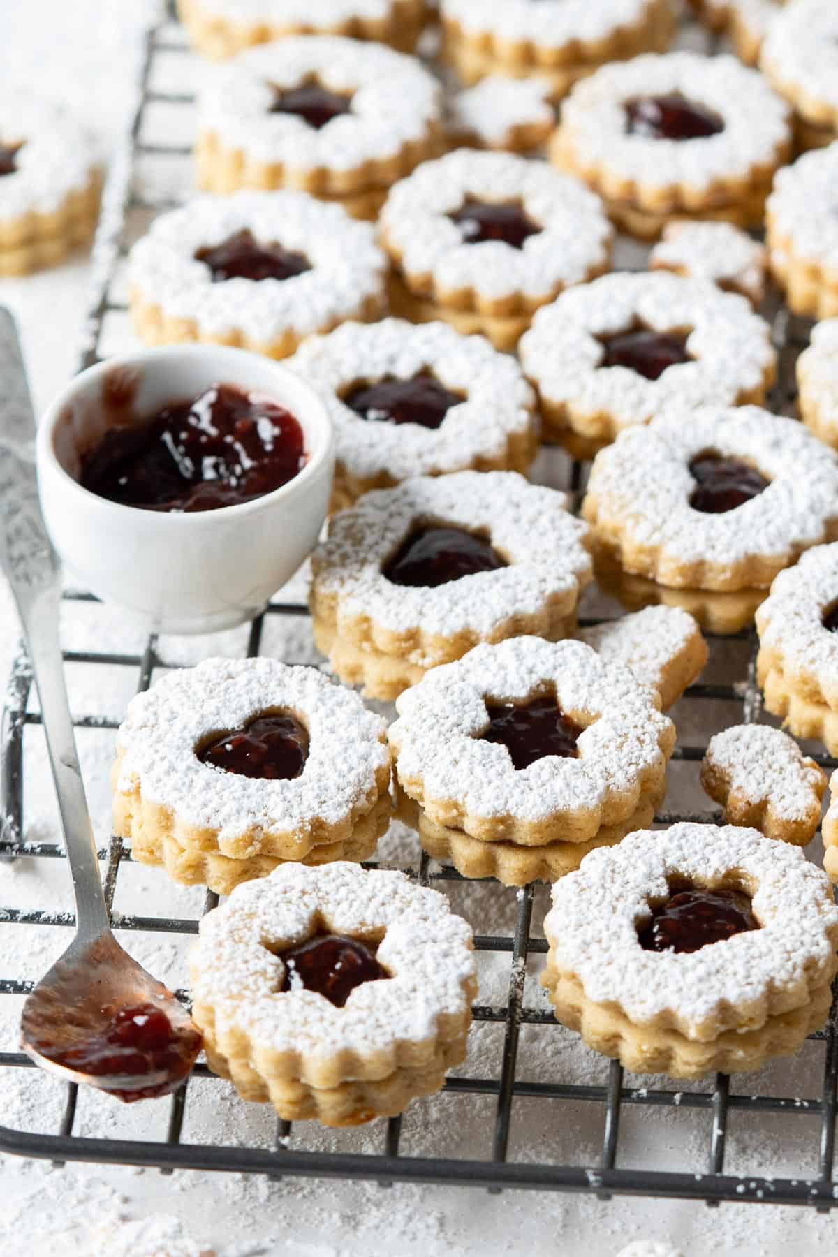 Healthy Linzer cookies on a cooling rack with a bowl of jam.