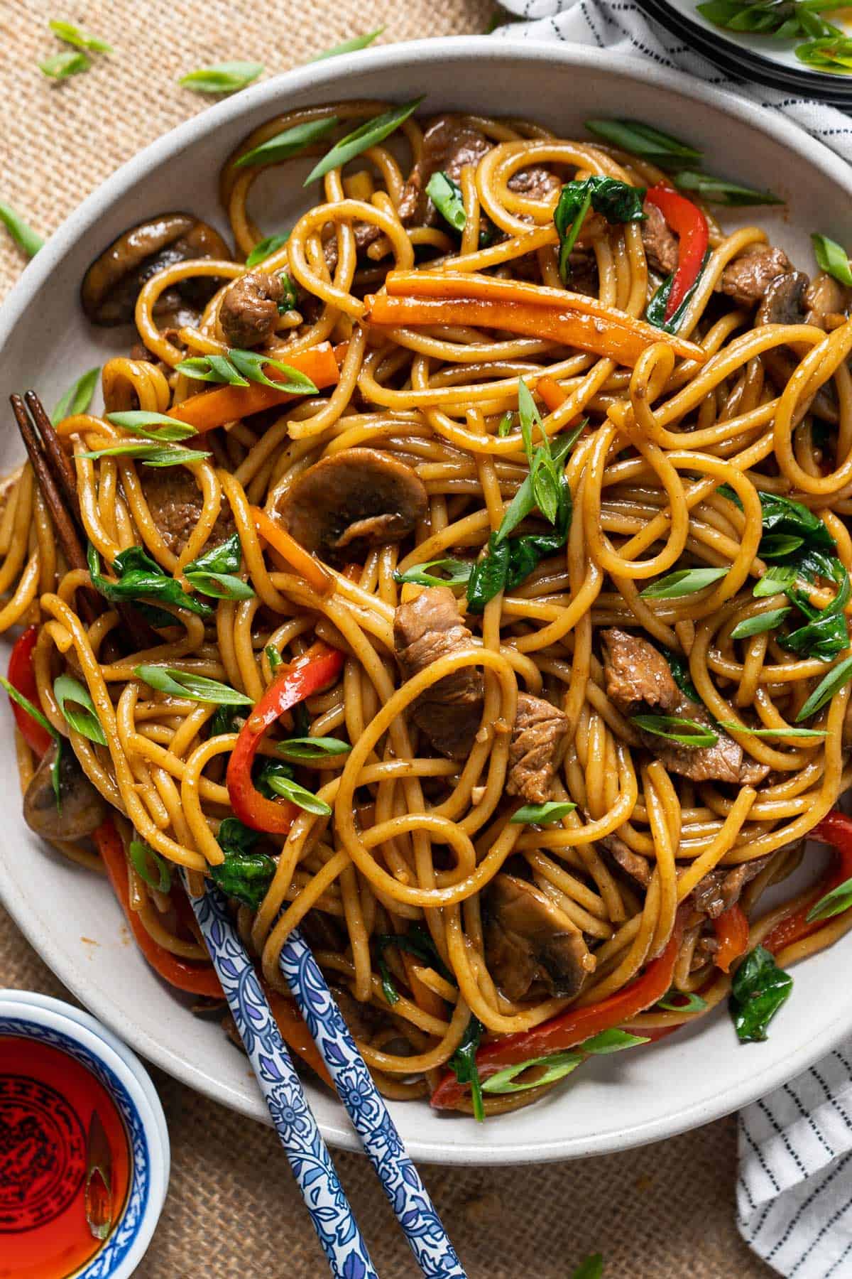 A plate of lo mein noodles with chopsticks.