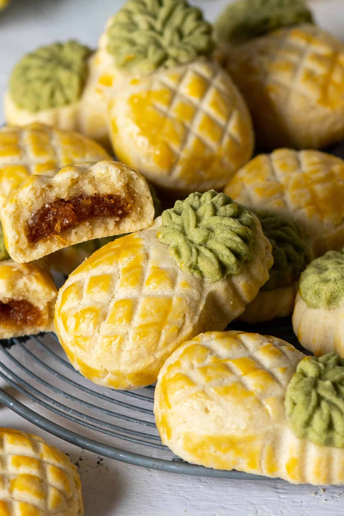 Pineapple tart cookies on a rack with one half eaten cookie on top.