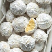 Snowball cookies in a bowl with one half eaten cookie on top.