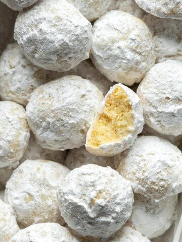 Snowball cookies in a bowl with one half eaten cookie on top.