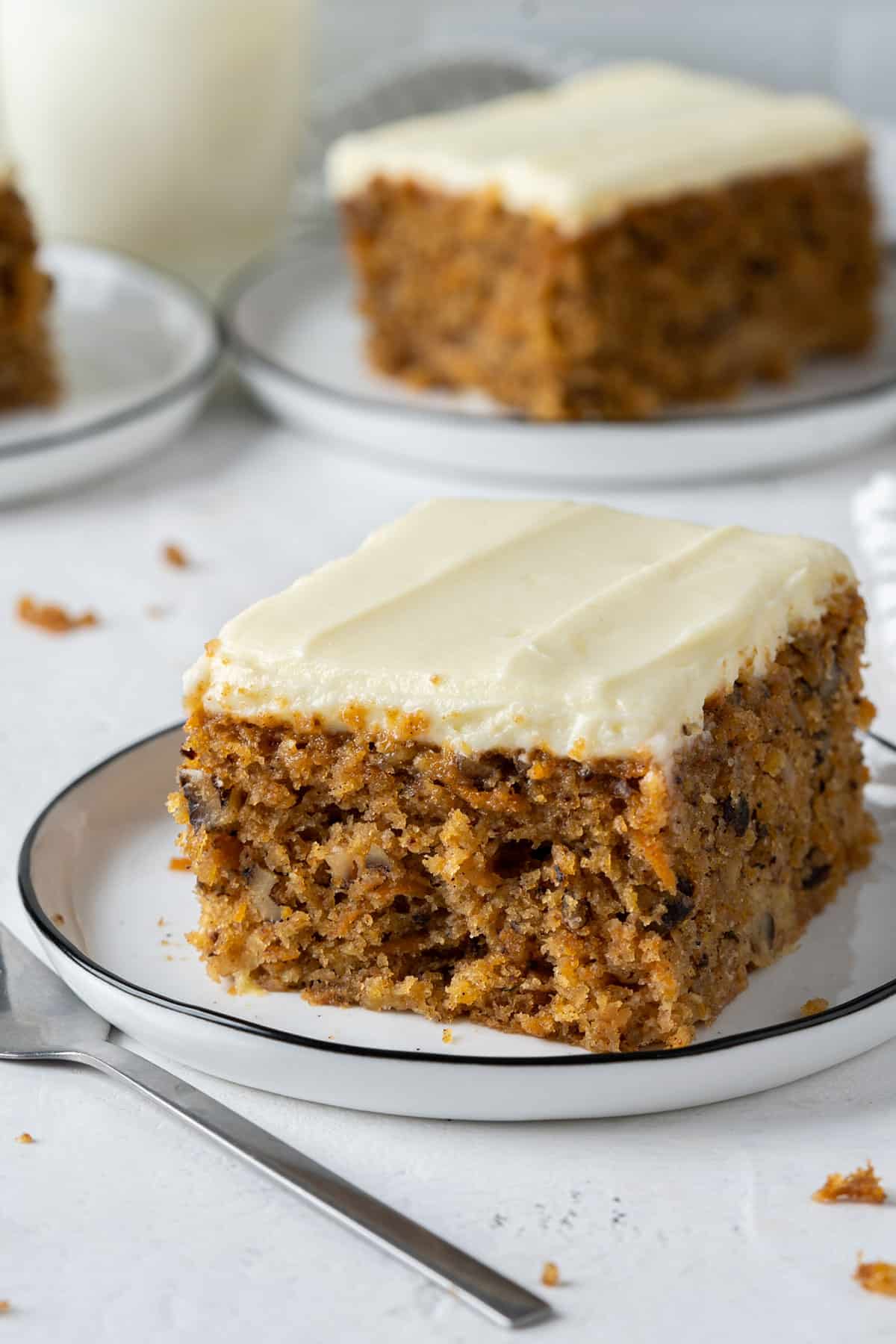 Two slices of carrot cake with pineapple on individual plates.