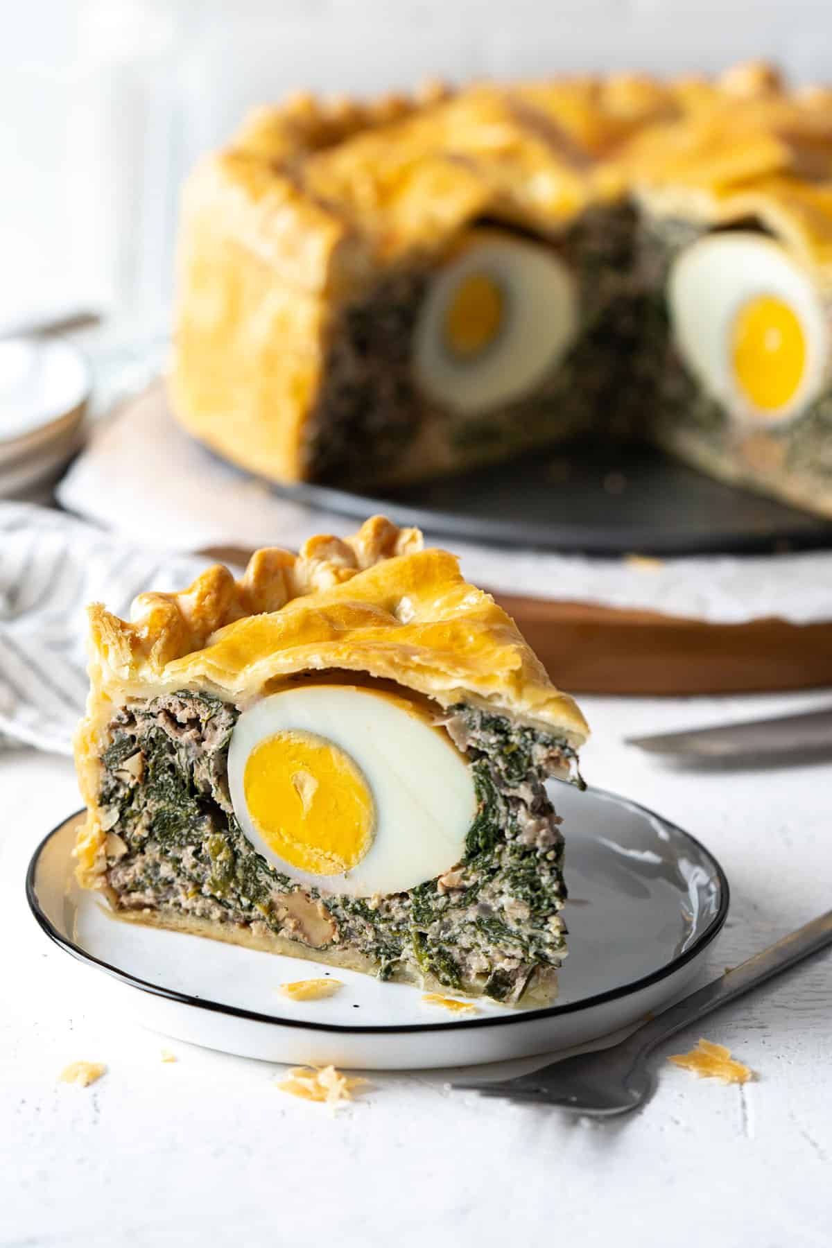 A slice of spinach ricotta pie on a plate with the whole pie in the background.