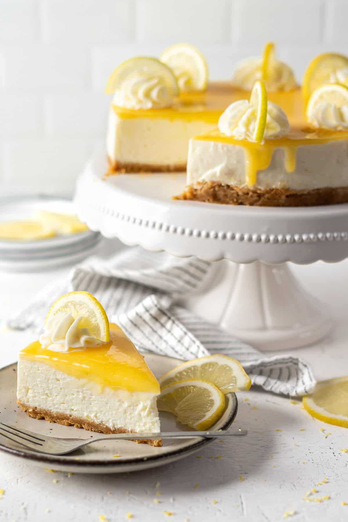 No-bake lemon cheesecake on a cake stand and a slice on a plate.