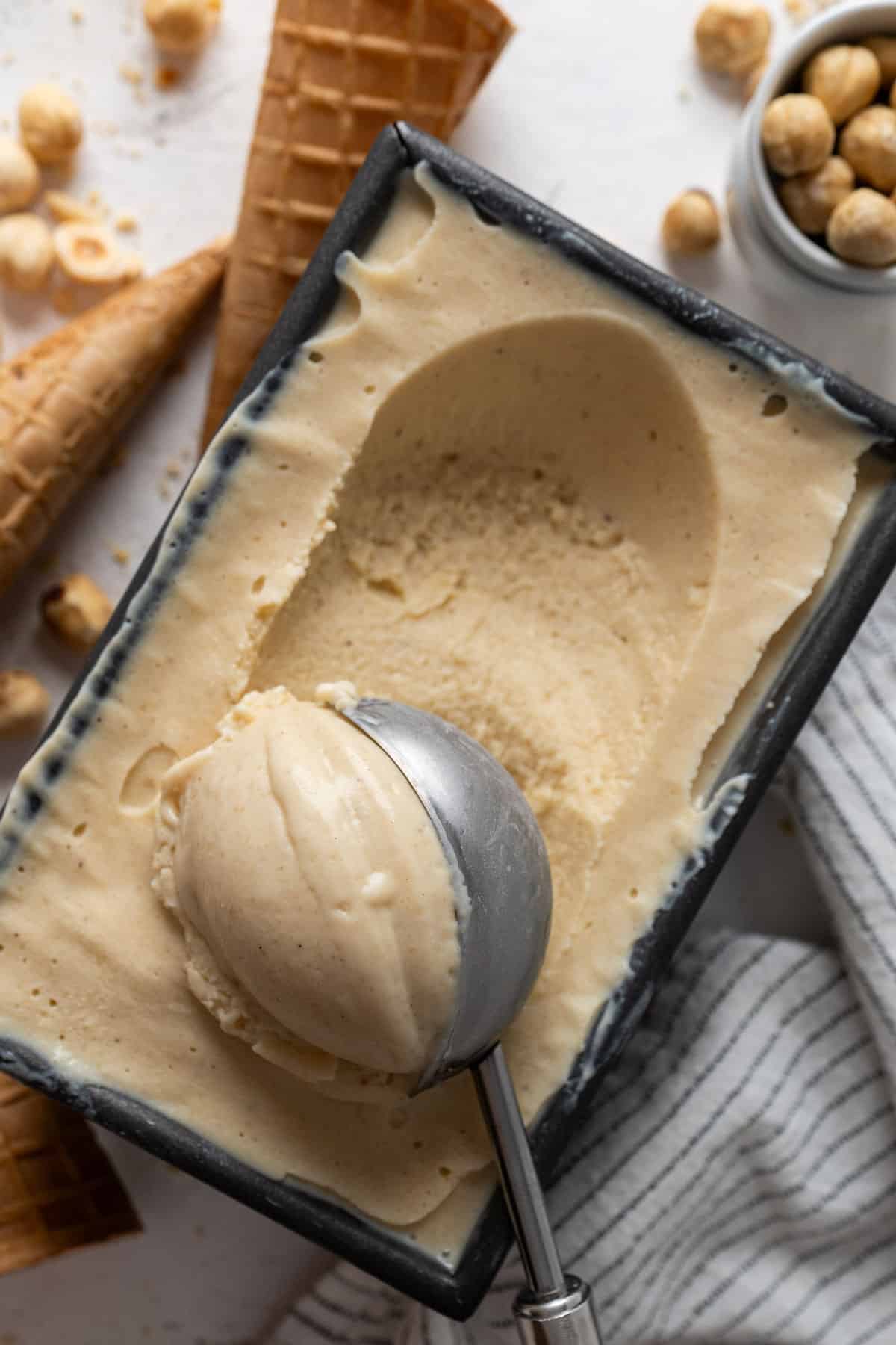 Scooping hazelnut ice cream from a tin.