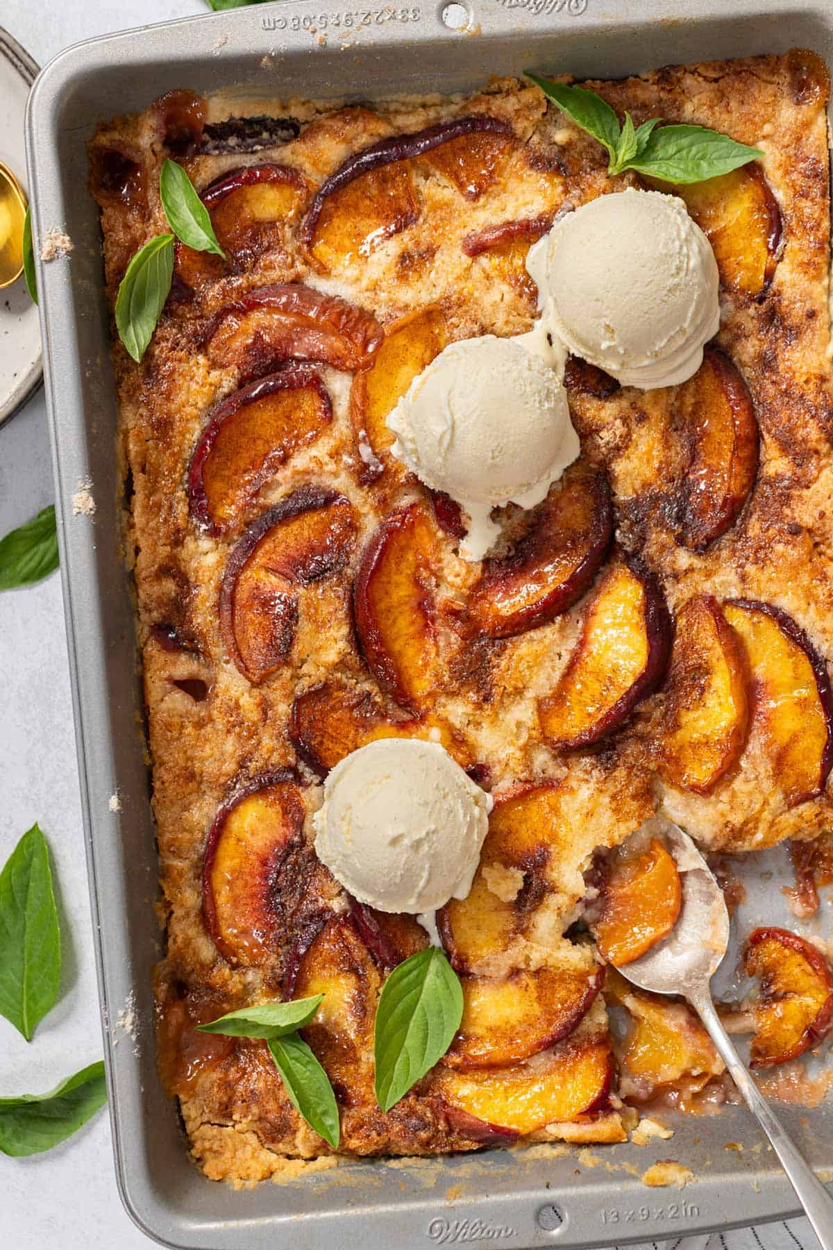 Peach cobbler with cake mix in a tray with scoops of ice cream.