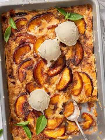 Easy peach cobbler with cake mix in a tray with ice cream.