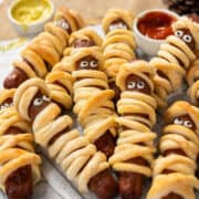 Hot dog mummies on a wooden plate.