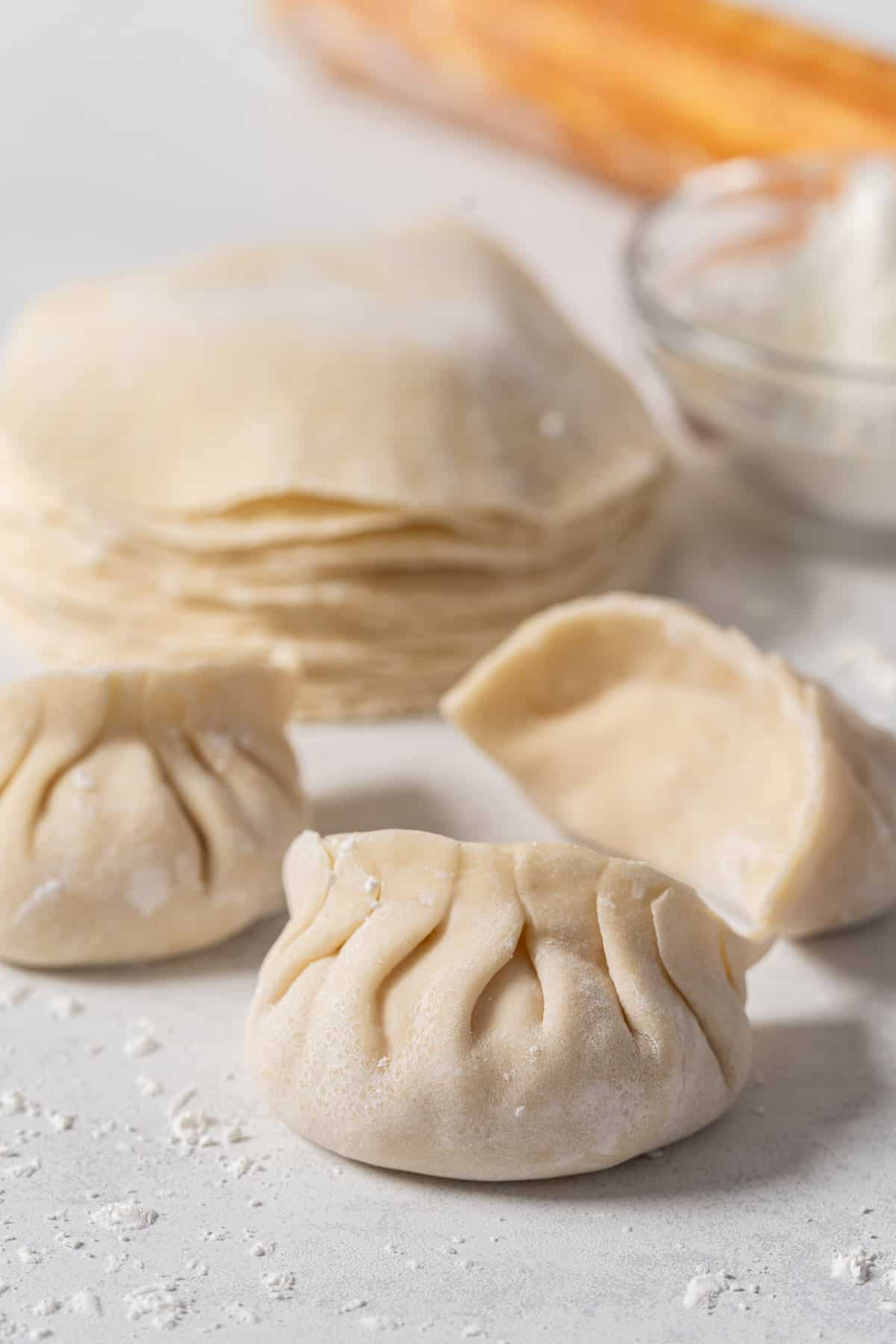 Filled dumplings with a stack of dumpling wrappers at the back.