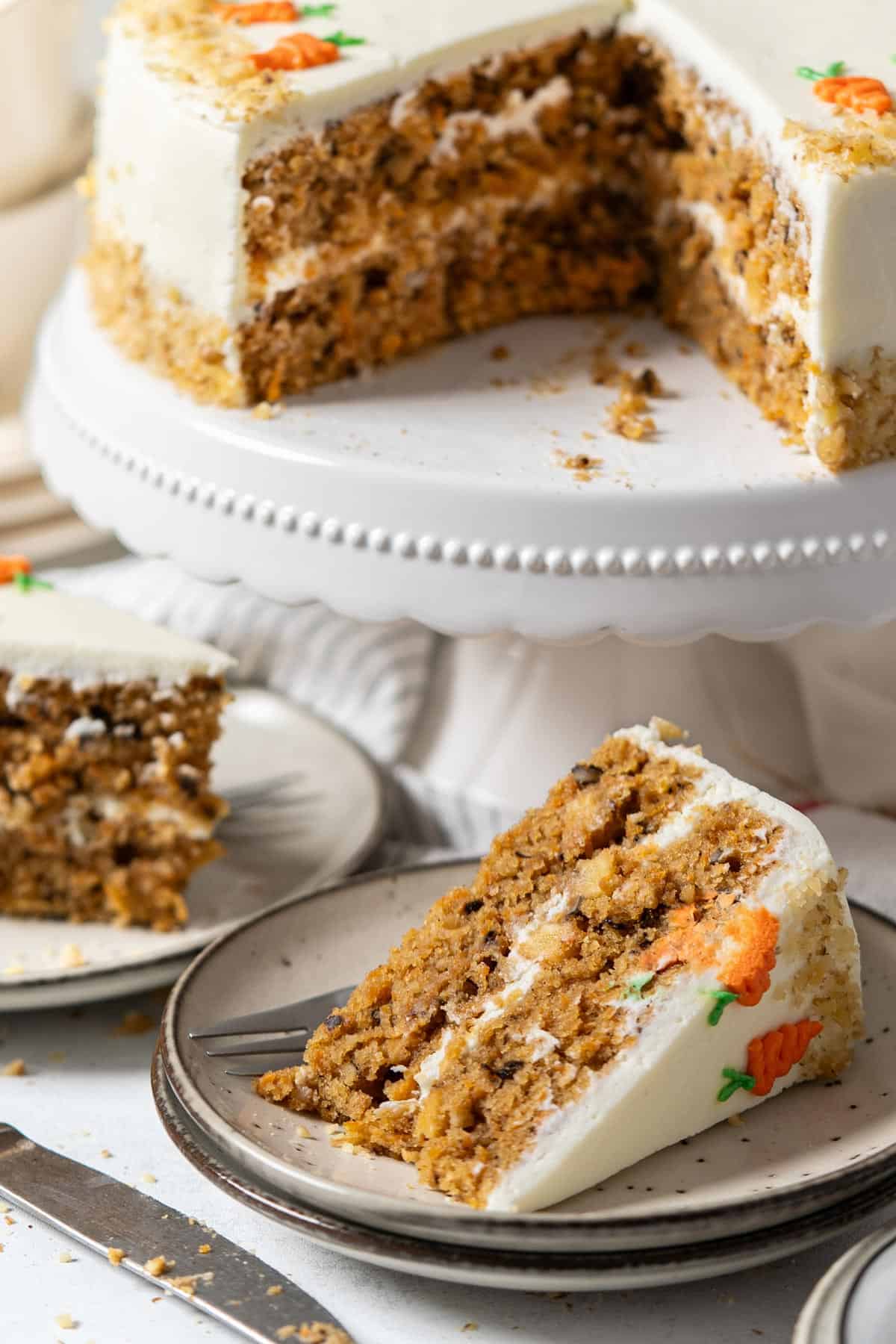 A portion of carrot cake in front of a cake stand.