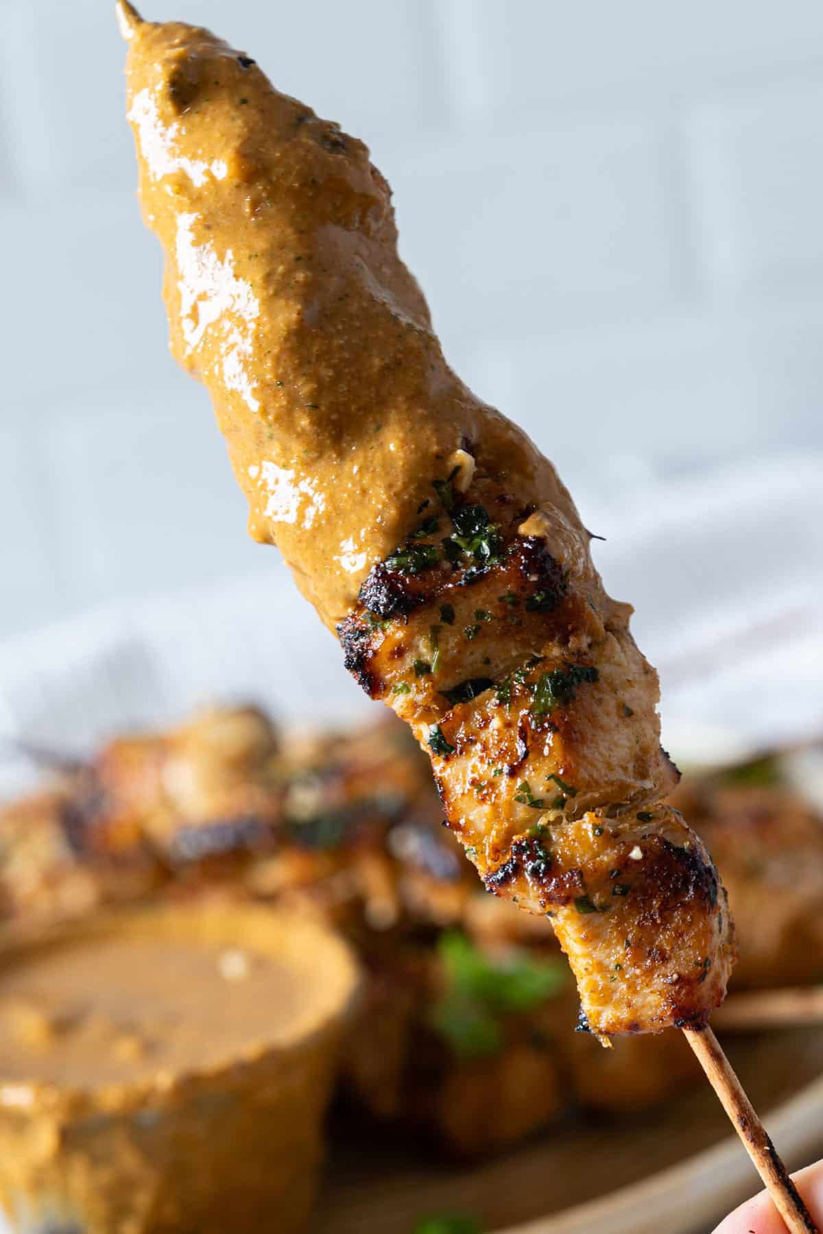 Holding a piece of chicken skewer dipped in peanut sauce.