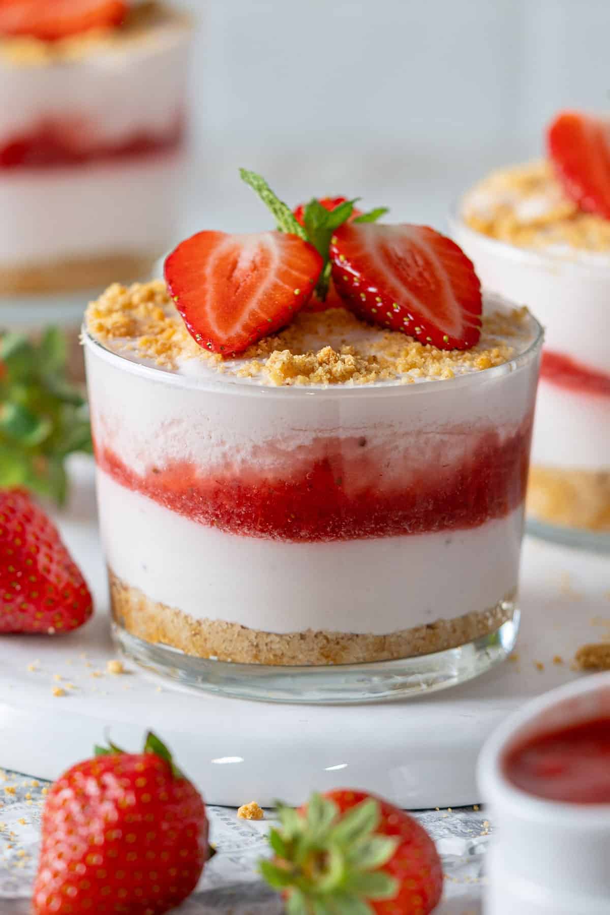 Strawberry cheesecake cups with strawberries all around.