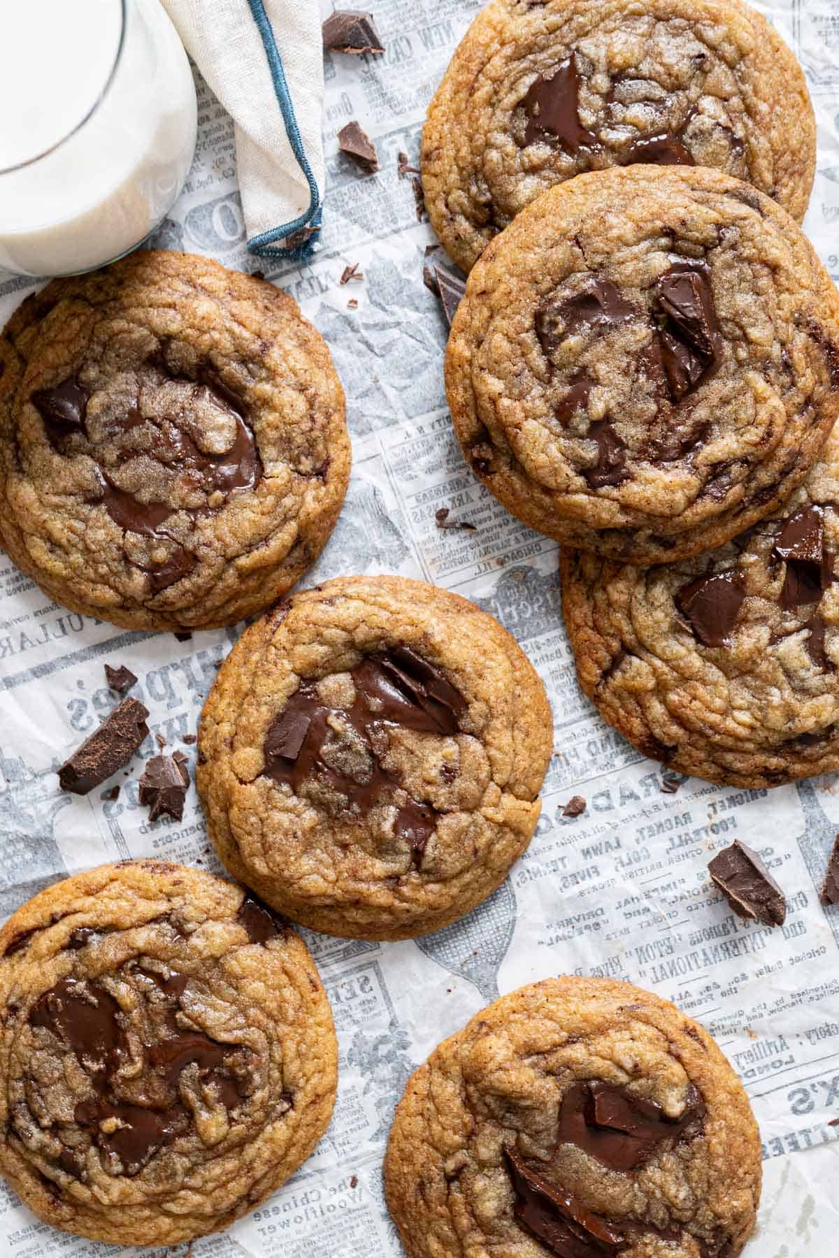 Chewy chocolate chunk cookies on a parchment paper with a glass of milk on the side.