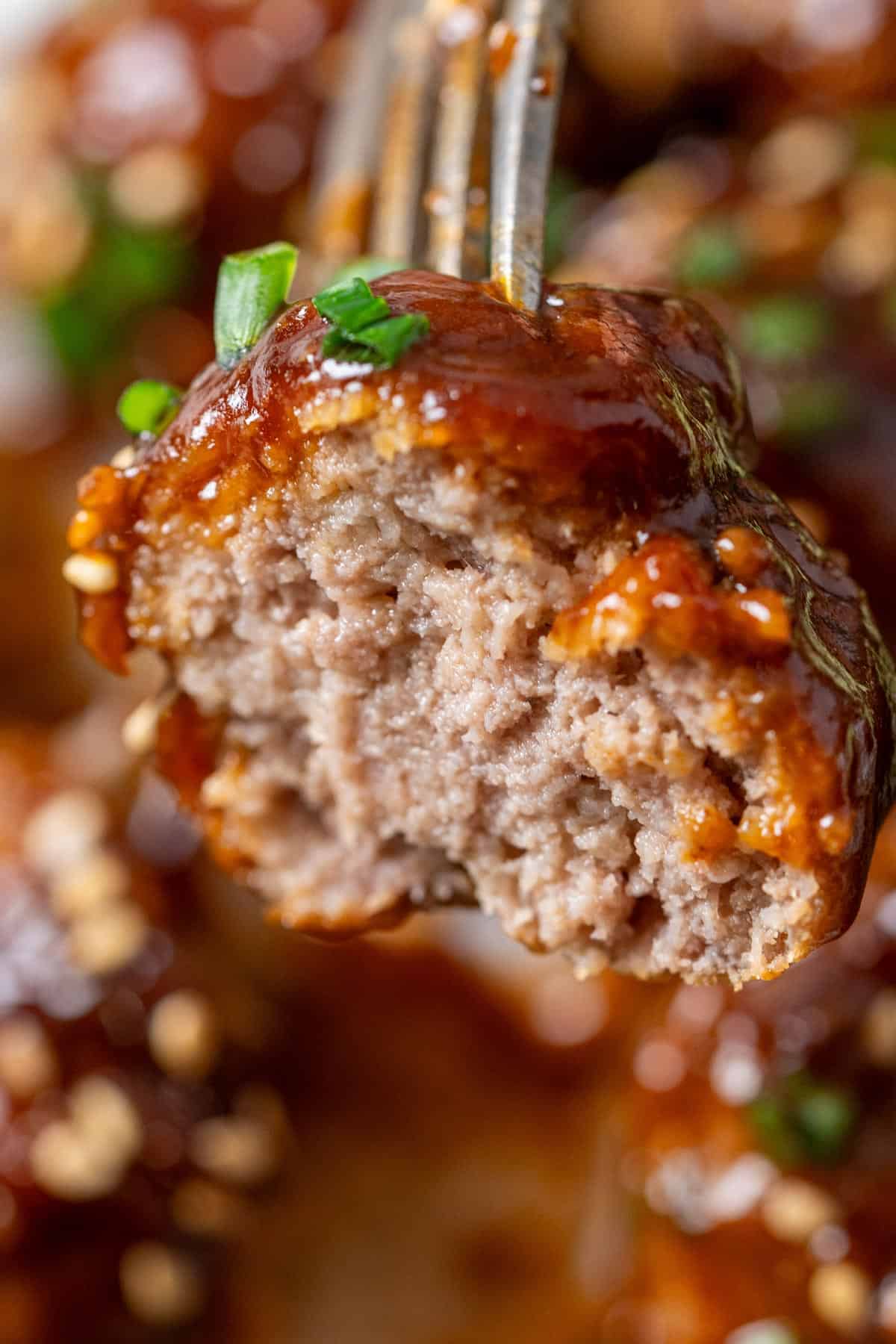 Holding a half eaten Korean BBQ meatballs with a fork showing the juicy inside texture.