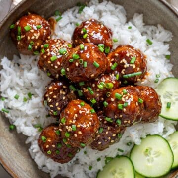 Korean meatballs on a bed of rice and sliced cucumber on the side.