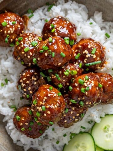 Korean meatballs on a bed of rice and sliced cucumber on the side.