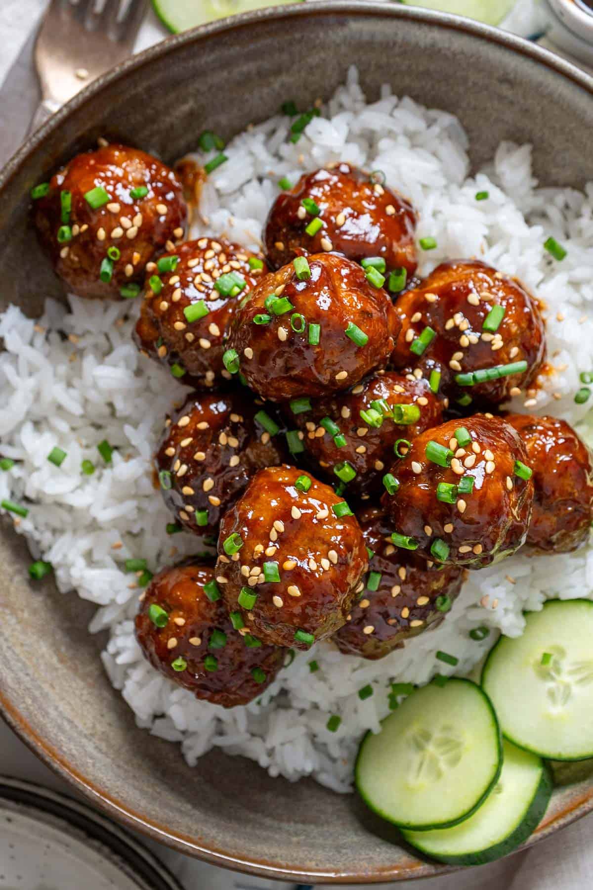 Korean meatballs on a bed of rice and some cucumber slices on the side.