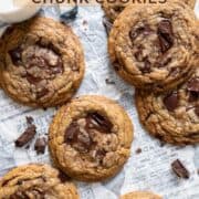 Seven chewy chocolate chunk cookies with a glass of milk on the side.