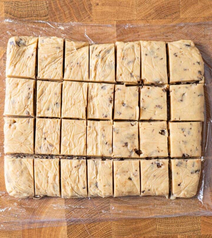 Cutting frozen cookie dough slab into portions for bottoms and tops.