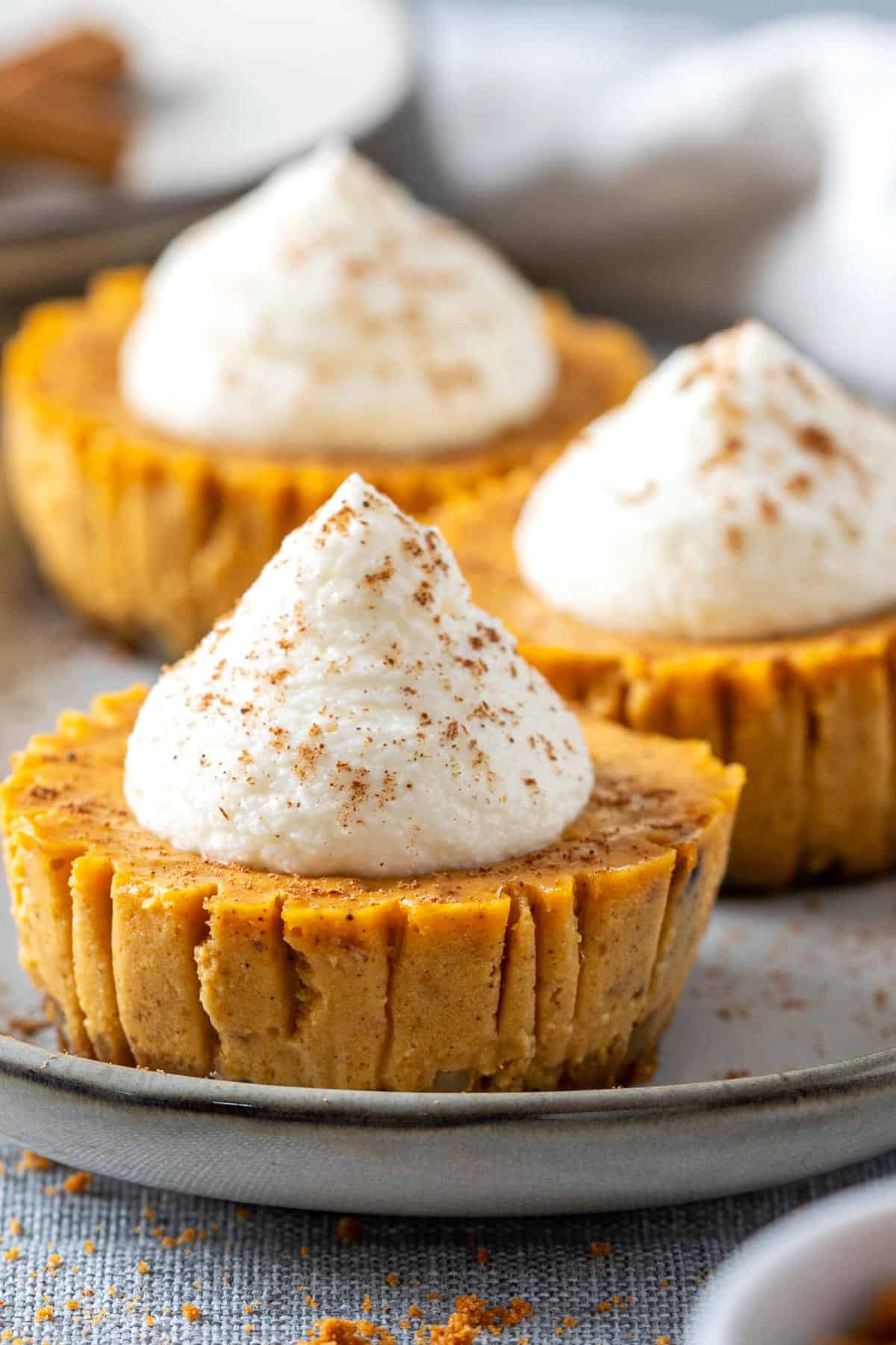 Mini pumpkin cheesecakes with whipped cream on a plate.