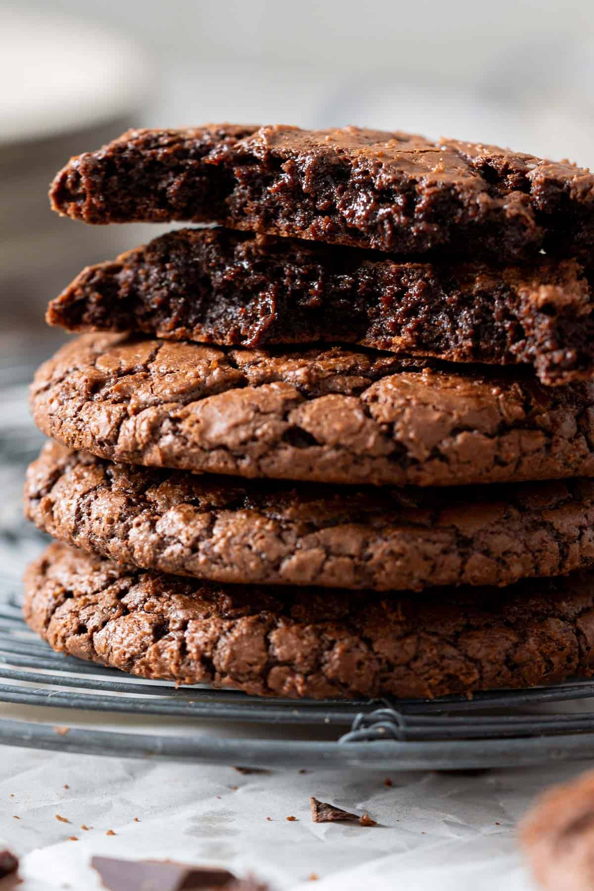 Stacked brownie cookies and one broken in half showing its fudgy texture.