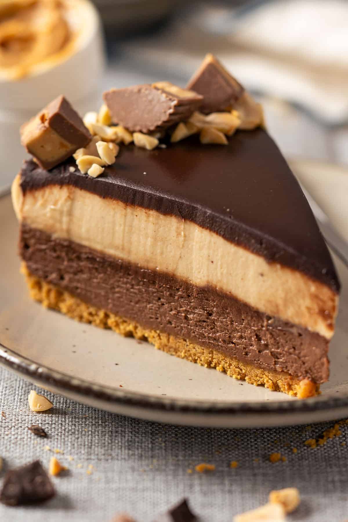 A slice of no bake peanut butter chocolate cheesecake on a plate topped with ganache and peanut butter cups.
