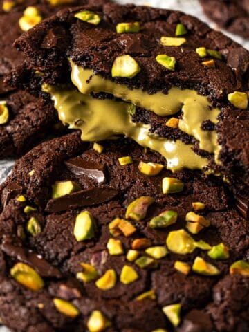 Chocolate pistachio cookie broken open with gooey pistachio cream filling and fudgy brownie-style texture.